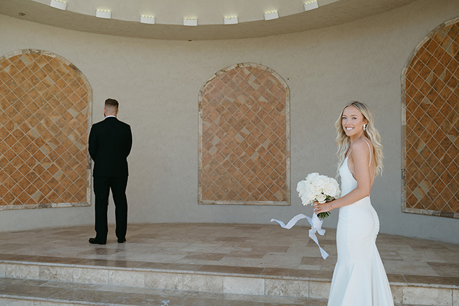 The bride smiling while the groom's back is turned before the first look. 