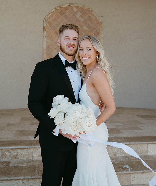 Bride and groom smiling while the bride holds an all-white bouquet. 