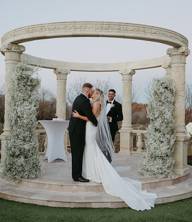 The bride and groom kissing at the altar with two baby's breath pillars. 