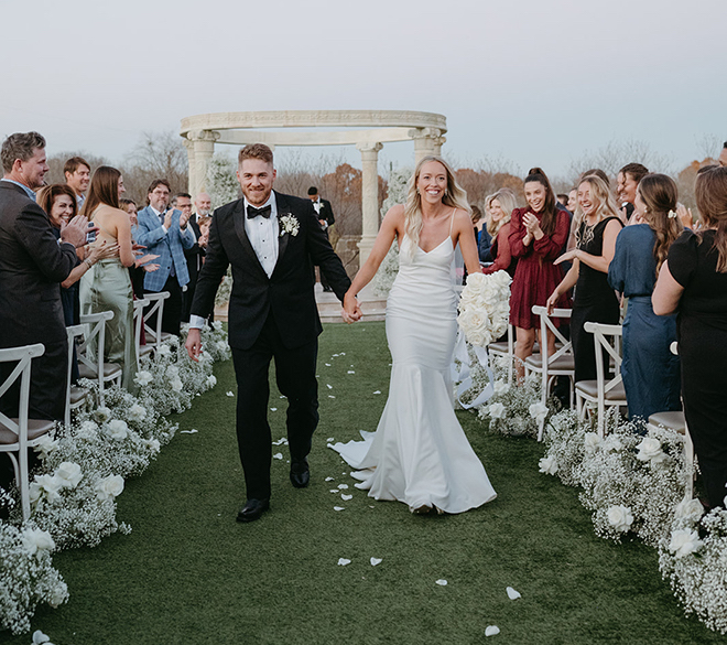 The bride and groom holding hands walking down the aisle dotted in baby's breath. 