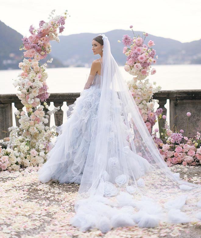 The bride standing in between the white and pink floral arrangement in her blue gown and veil. 