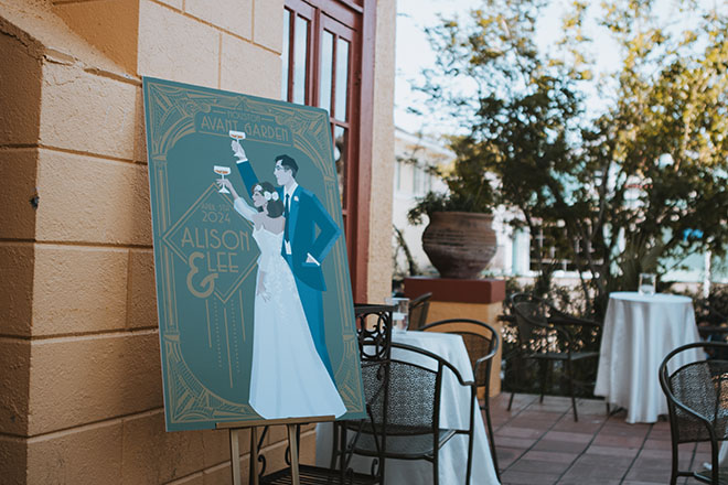 A 1920s themed poster greets guests for the cocktail hour at their art nouveau wedding.