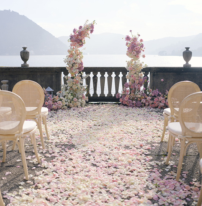 The ceremony site covered in flower petals, a white and pink floral arch and the view of Lake Como and the mountains. 