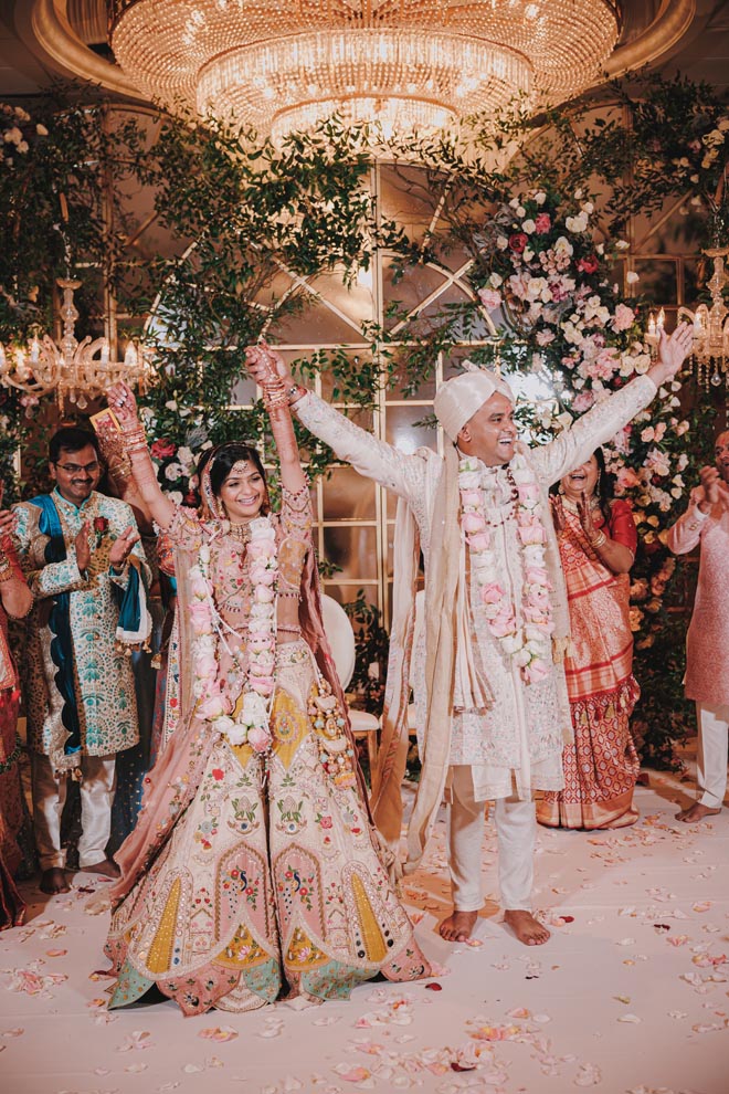 The bride and groom celebrate under their mandap detailed in pastel flowers.