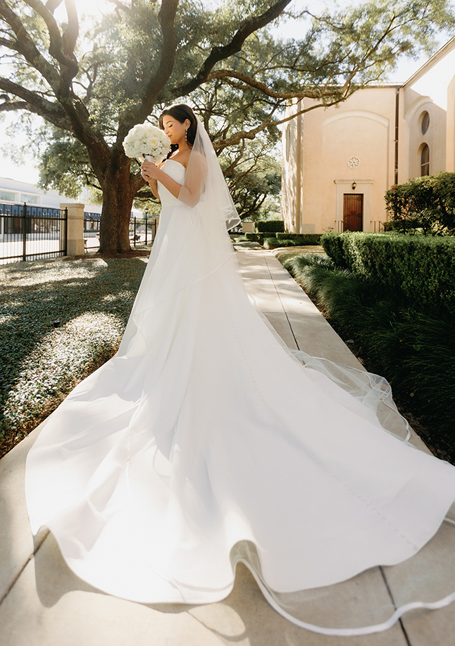 The bride smelling the white roses in her bouquet outside of the church. 