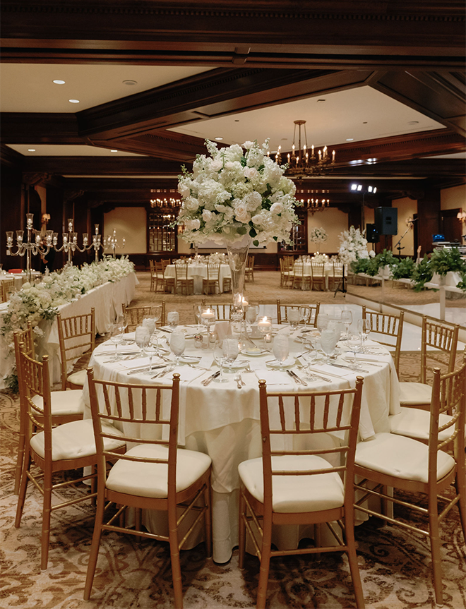 A round table with white linens and a white floral arrangement in the ballroom of The Houstonian Hotel, Club & Spa for a traditional wedding. 