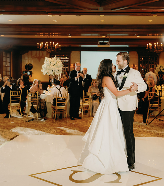 The bride and groom dancing on a custom white dance floor with an S in gold. 