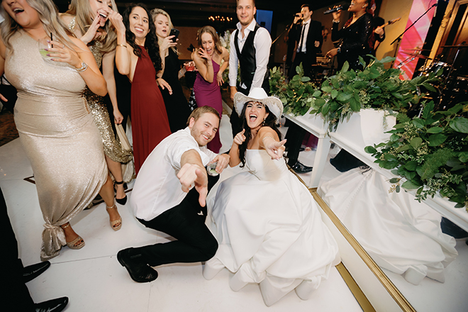 The bride wearing a white cowboy hat and a guest pointing at the camera on the dance floor. 