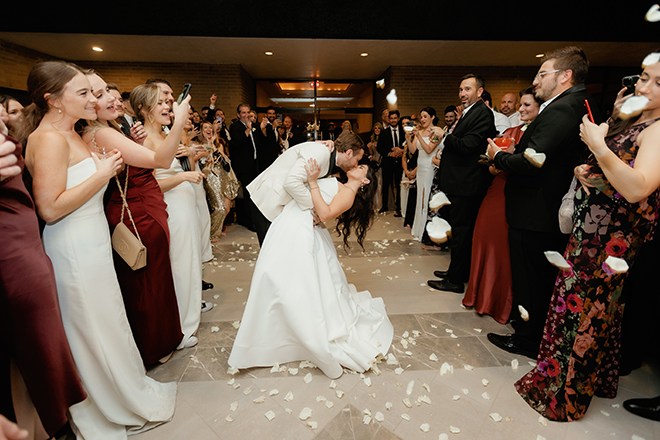 The bride and groom kissing while guests cheer and throw rose petals outside The Houstonian Hotel, Club & Spa. 