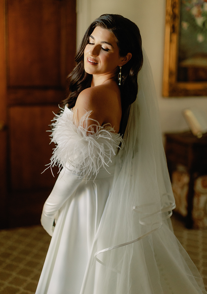 The bride wearing her veil, a strapless wedding gown and feathered gloves. 