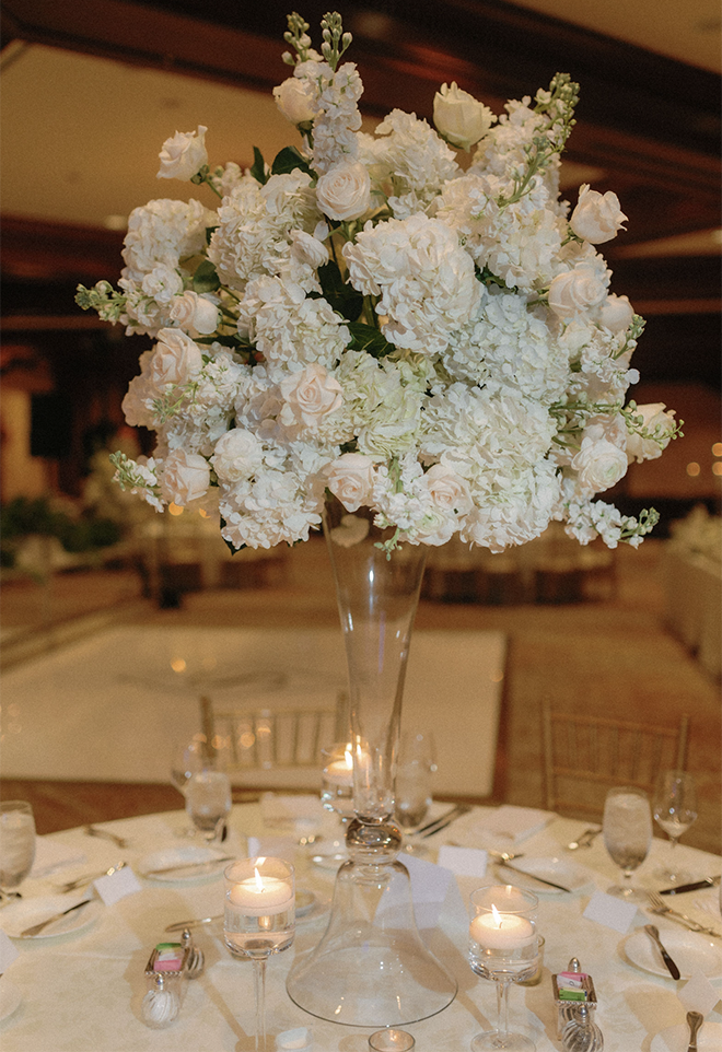 A round table with white linens and a white floral arrangement in the ballroom of The Houstonian Hotel, Club & Spa for a traditional wedding. 