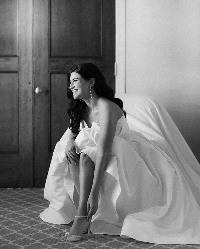 The bride wearing a strapless wedding dress putting on her lace heel. 