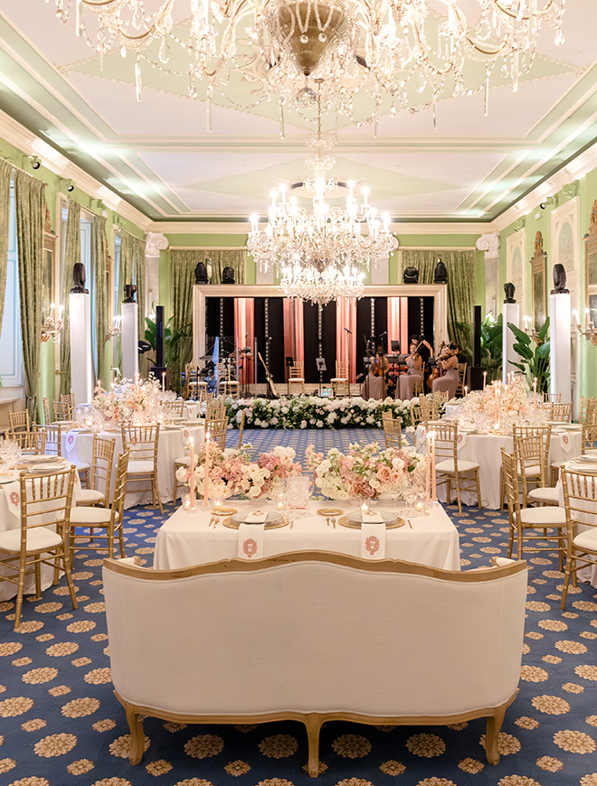 A green ballroom decorated with gold, white and blush reception decor. 