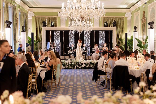 Wedding entertainment on the stage in the ballroom while guests sit at round tables. 