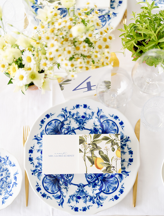 A white and blue printed plate with white and yellow florals and lemon place cards. 