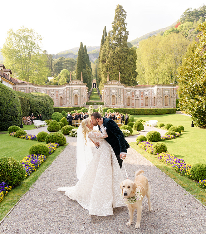 The bride and groom kissing in front of their ceremony space with a golden retriever by their side. 