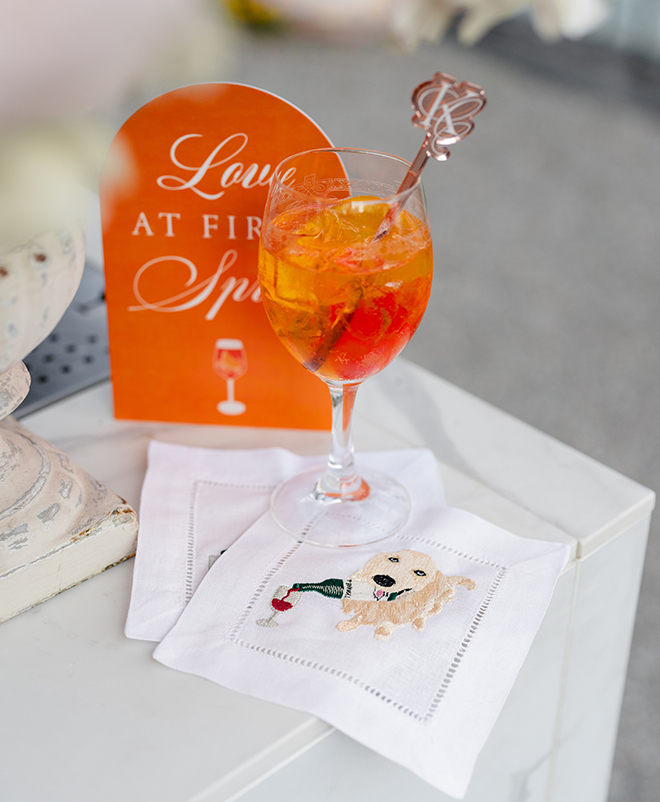 An aperol spritz sitting on a napkin with a golden retriever holding a wine bottle printed on it. 