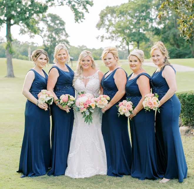 The bride and five bridesmaids in navy dresses posing on a golf course. 