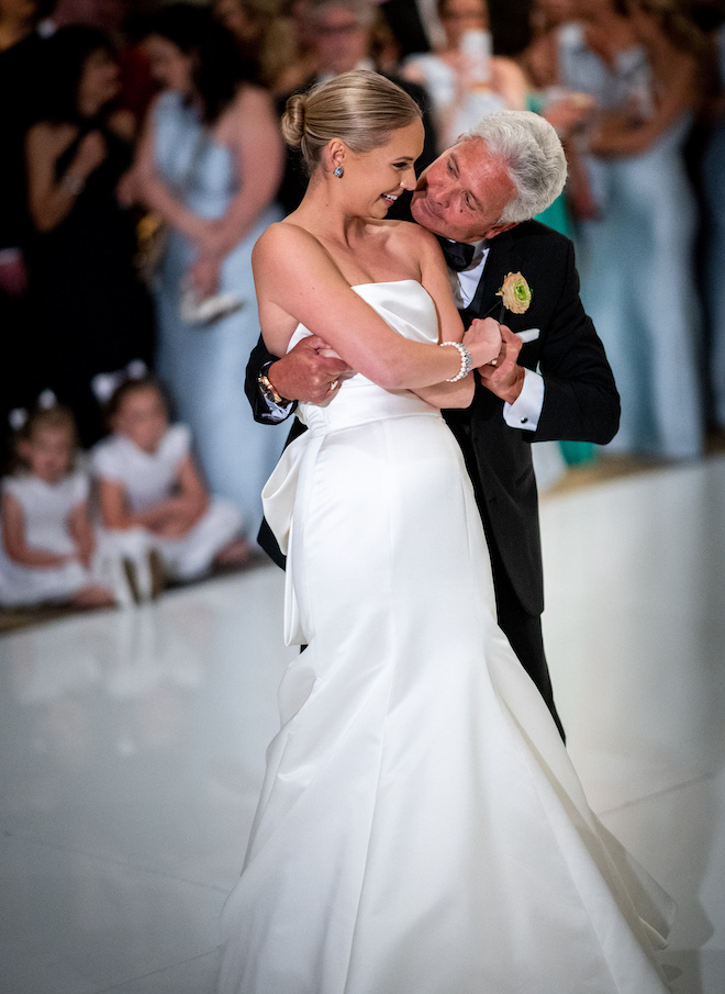 A bride's father leaning over her shoulder and smiling at her while they dance. 