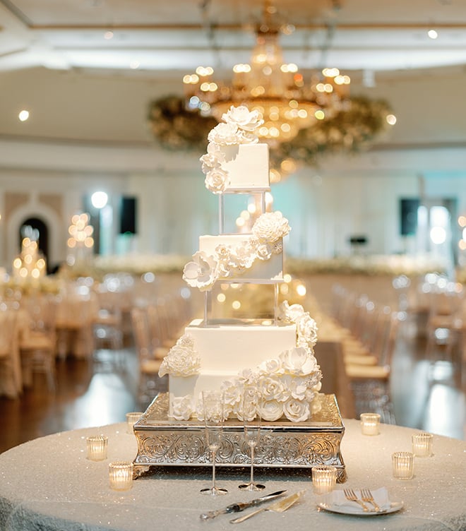 A wedding cake with alternating white and clear tiers garnished with florals. 