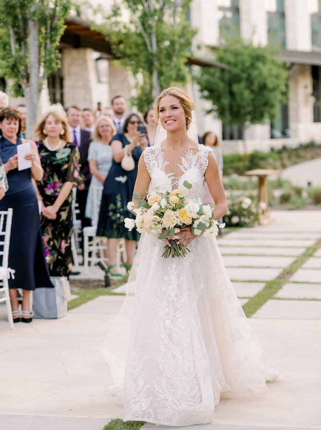 A bride walking down an outdoor aisle. 