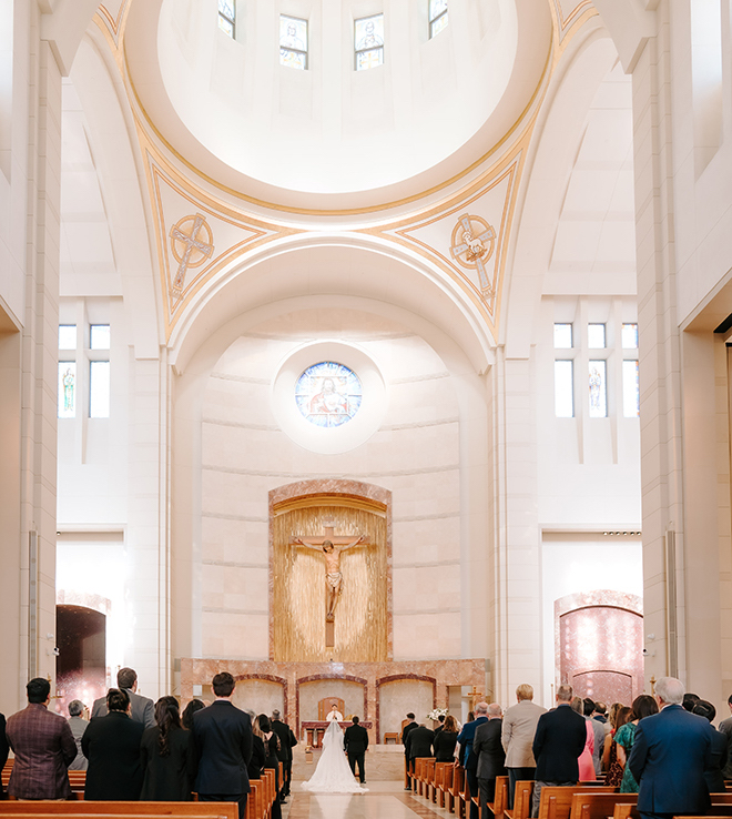 The bride and groom standing at the altar of the church with guests standing behind them in the pews. 