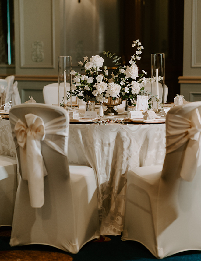 A round reception table with white linens, candles and a floral centerpiece. 