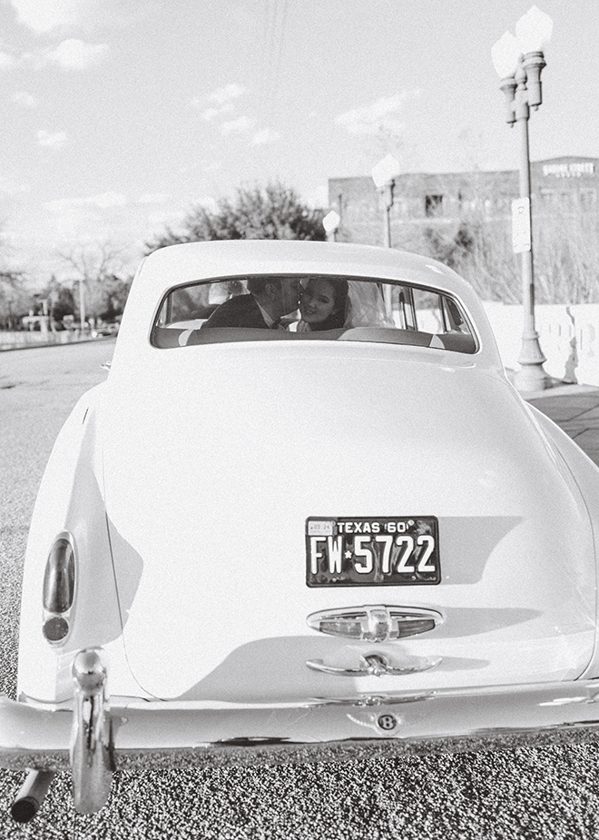 The groom kissing the bride's cheek in the back seat of the white vintage Bentley. 