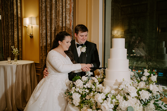 The bride and groom cutting into the 5-tier white wedding cake. 