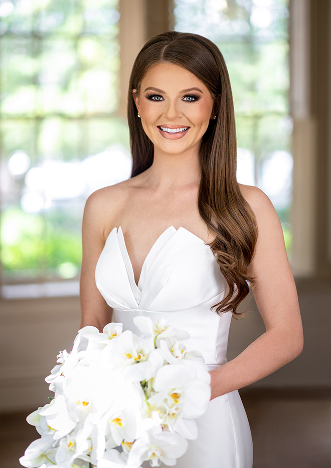 The bride smiles holding her wedding bouquet of orchids.