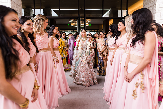 The groom smiling with her bridesmaids in pink standing in front of her. 