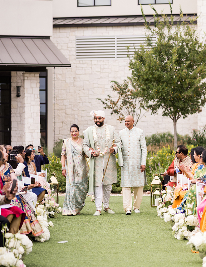 The groom walking down the aisle with his parents. 