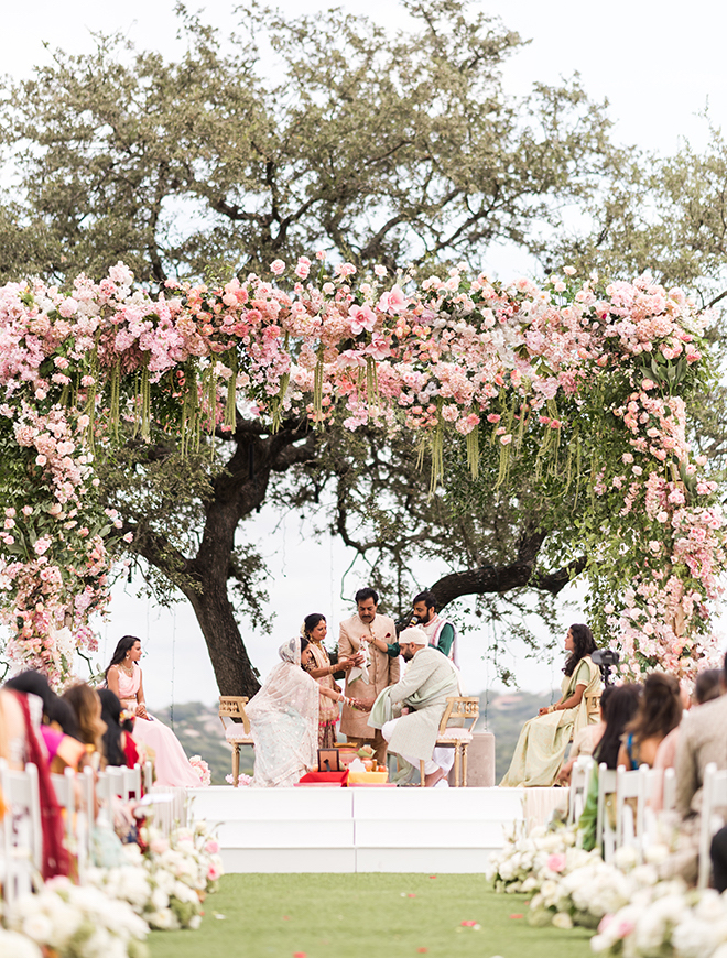 Bride and groom sitting under a mandap covered in pink flowers and greenery at Omni Barton Creek Resort & Spa.