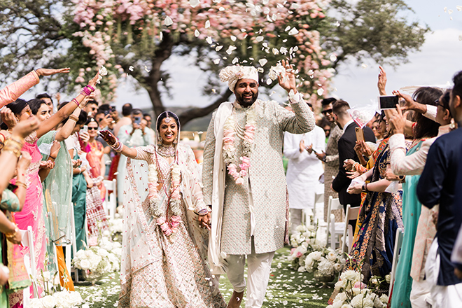 The bride and groom holding hands walking back down the aisle with guests throwing flower petals at them. 