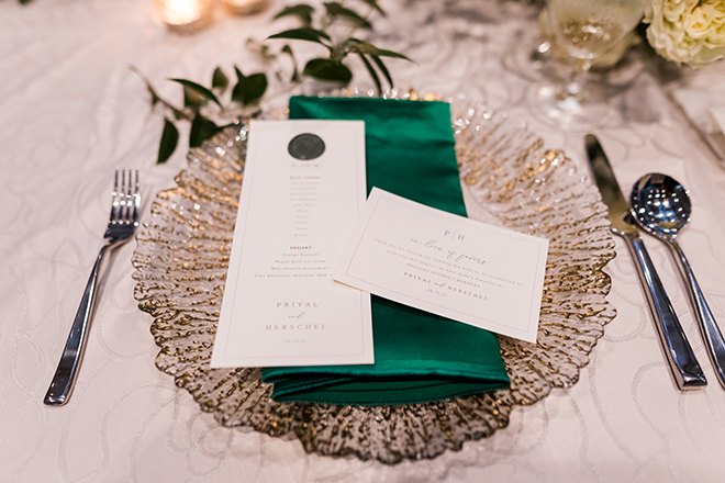 A white menu with a green napkin and shiny gold plate. 