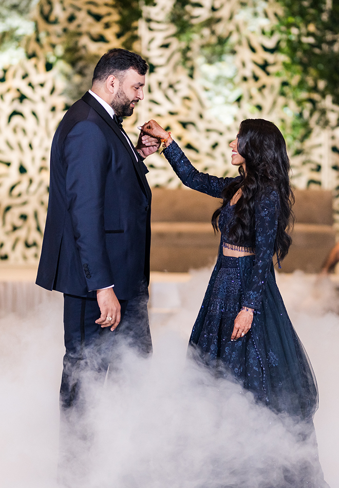 A bride and groom holding hands on the dance floor with smoke at their feet. 