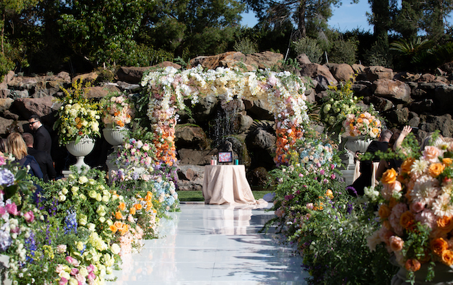 A ceremony set up with a large flower arch and colorful flowers lining the aisle. 