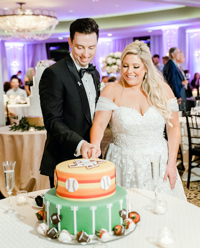 The bride and groom smile happily as they cut into the groom's cake at their wedding reception. 