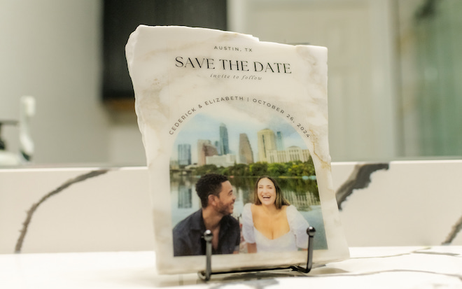 A white and grey marble plaque with a "save the date" details and photo of a happy couple. 