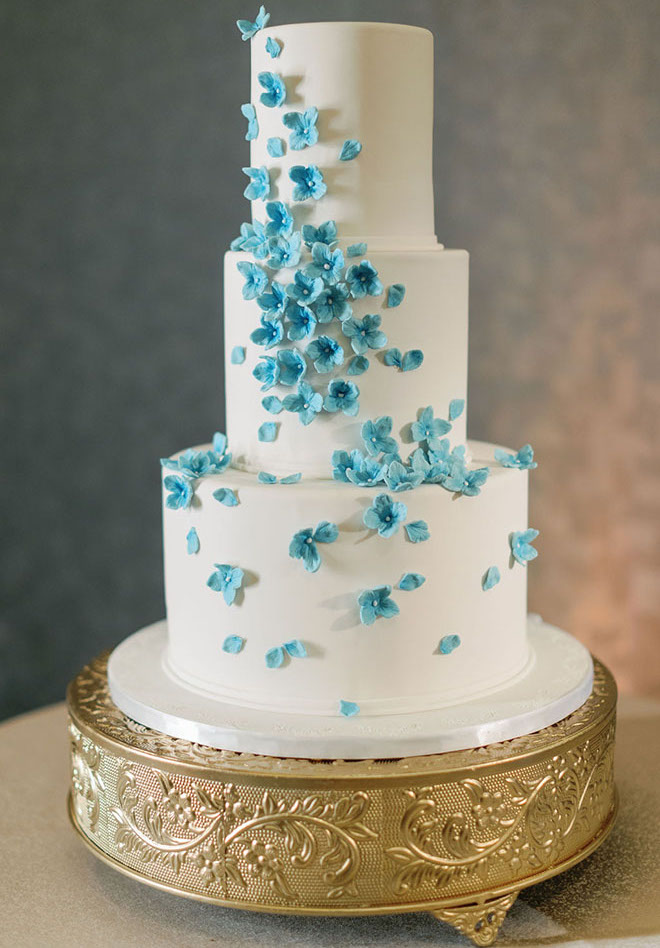 Cakes by Gina creates a three-tier white wedding cake adorned in blue flowers.