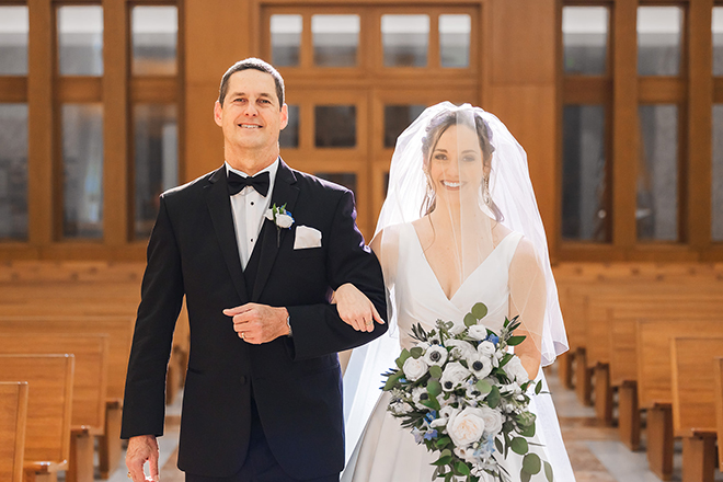 The bride's dad walks her down the aisle hand and hand with her floral bouquet. 