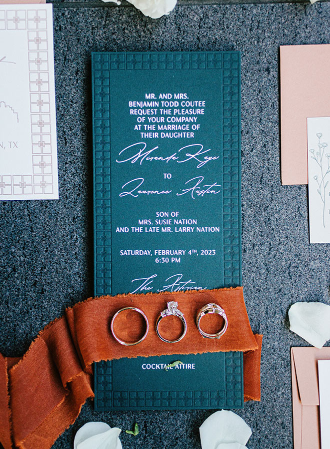 The wedding bands lay on top of emerald green and pink wedding stationery.