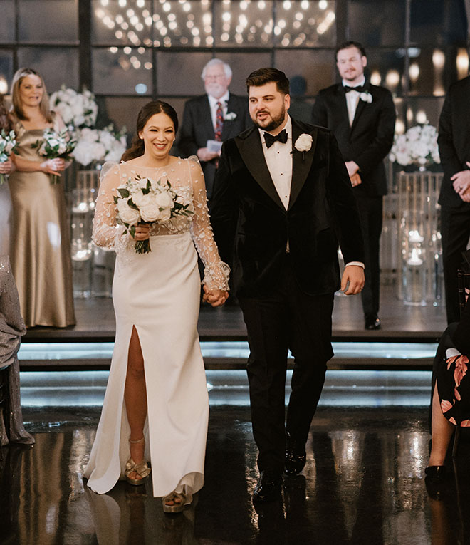 The bride and groom walk down the aisle holding hands. 