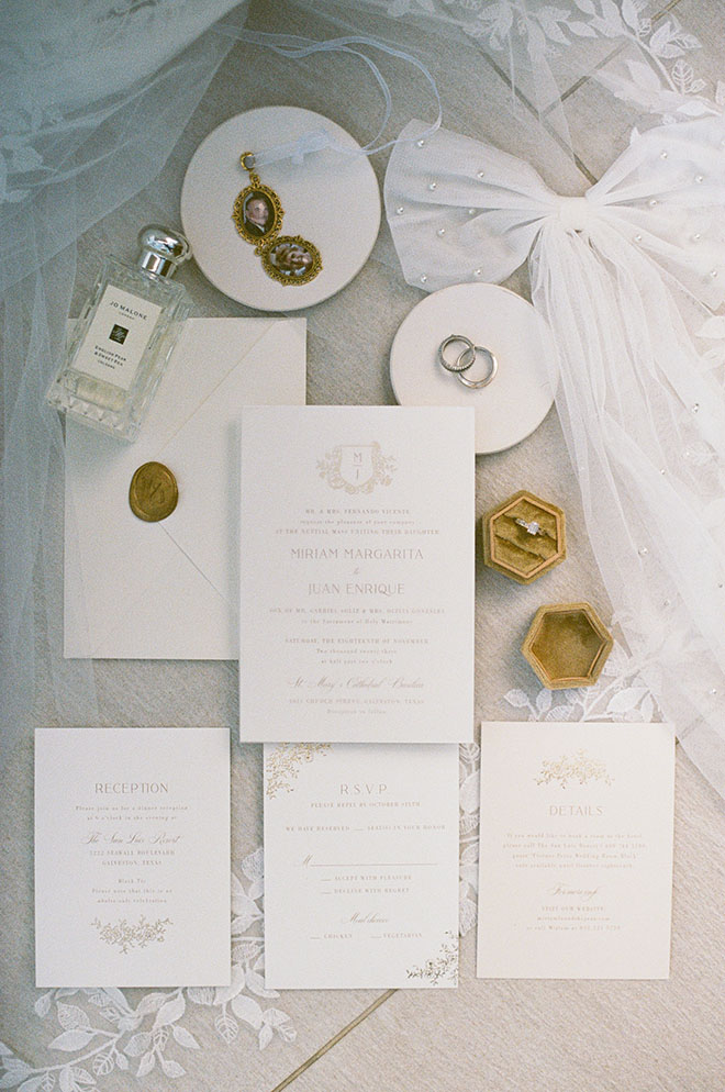 White and gold wedding stationery and invitations lay next to the bride's perfume an jewelry.