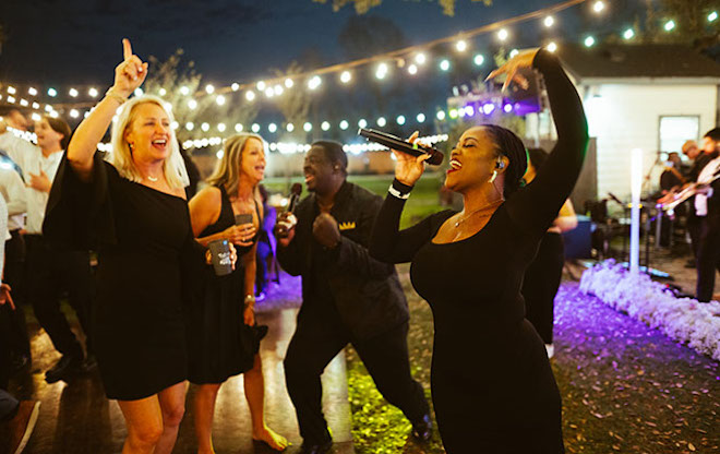 The live band sings in her microphone as guests sing with her as their hands are up in the air. 