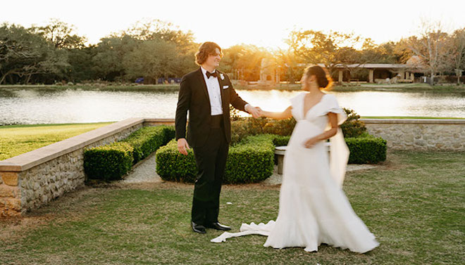 The bride and groom take photos in a dancing motion at sunset with the lake behind them. 