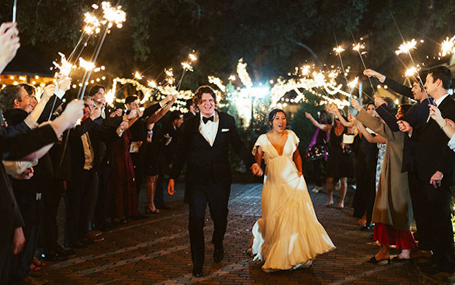 The bride and groom leave the reception as their guests hold up sparklers. 