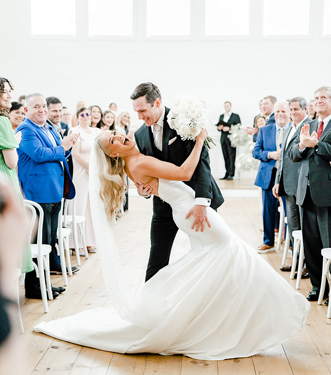 The groom dips the bride at the end of the alter with smiles on their faces. 