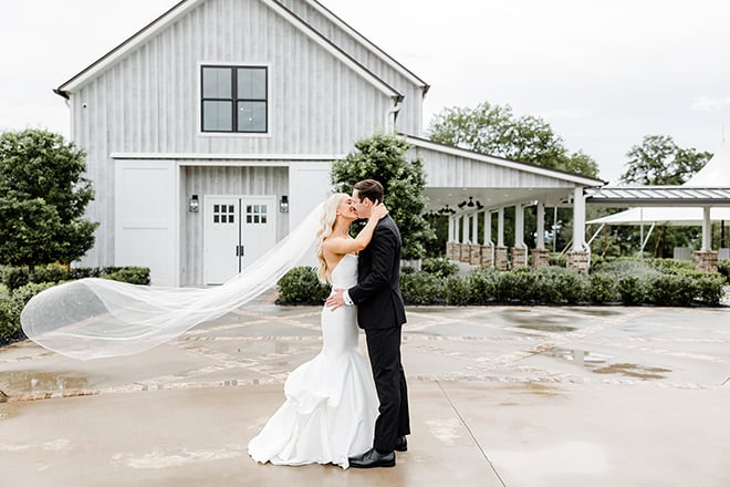 Bride and groom hug close as they pose for the photo infront of the venue. 