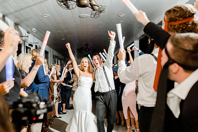 The bride and groom are doing send off as their guests cheer them on with neon lights. 